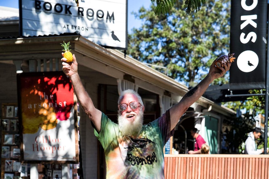 An old man holding a pineapple uses a hula hoop