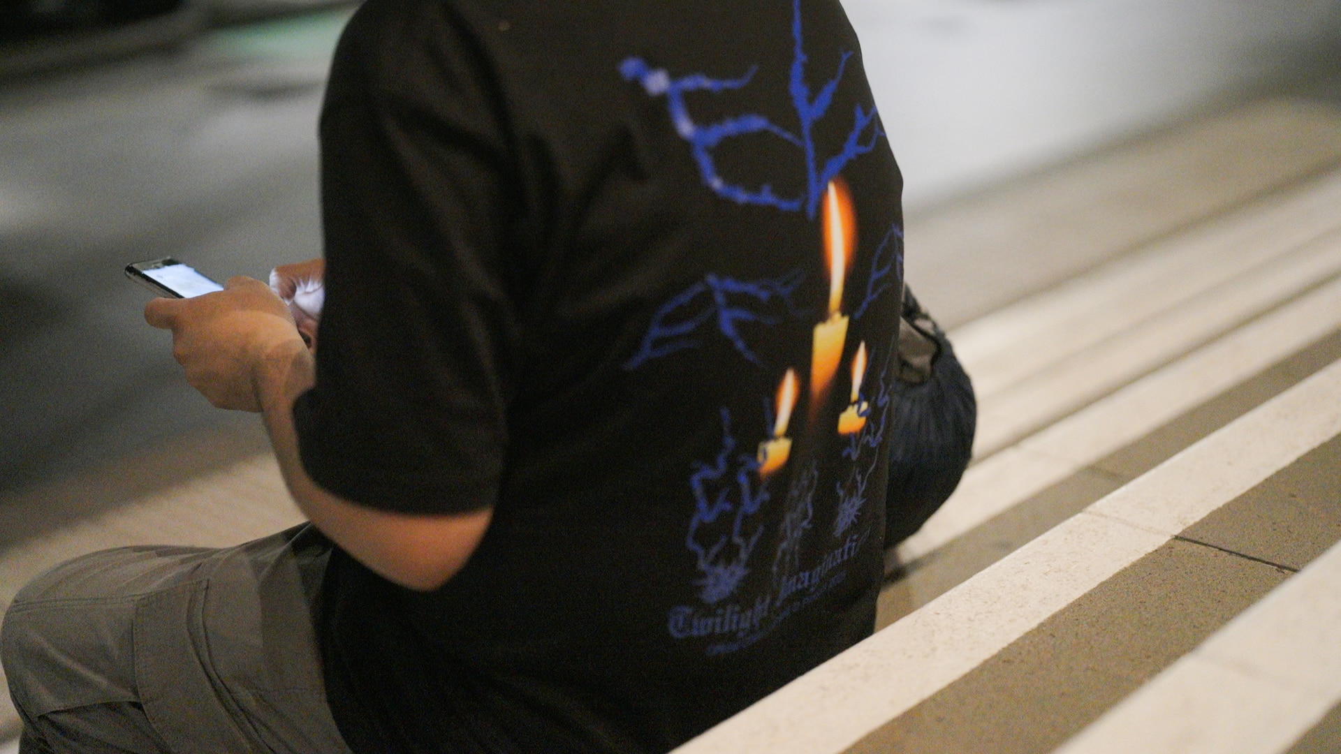 A man sits outide on steps looking at his phone.