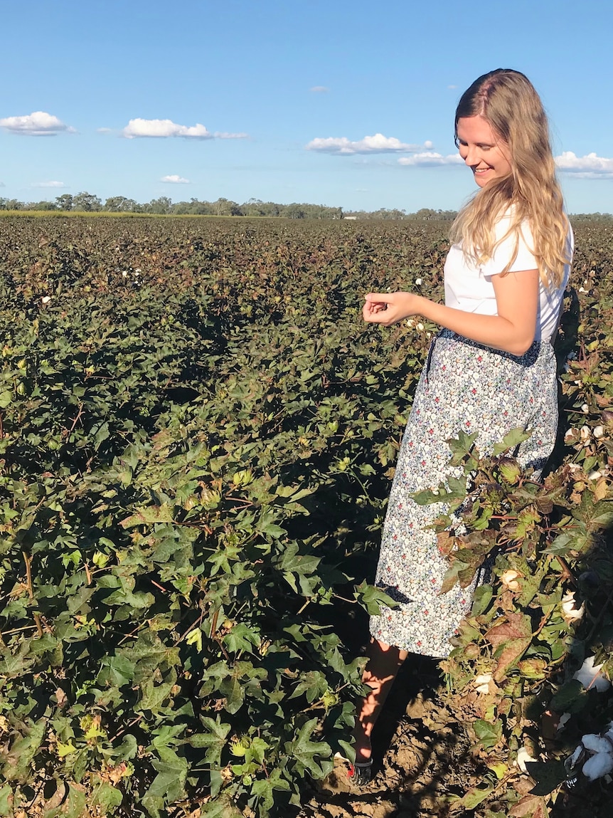 Emma Bond stands in a cotton field, trees are visible in the background.