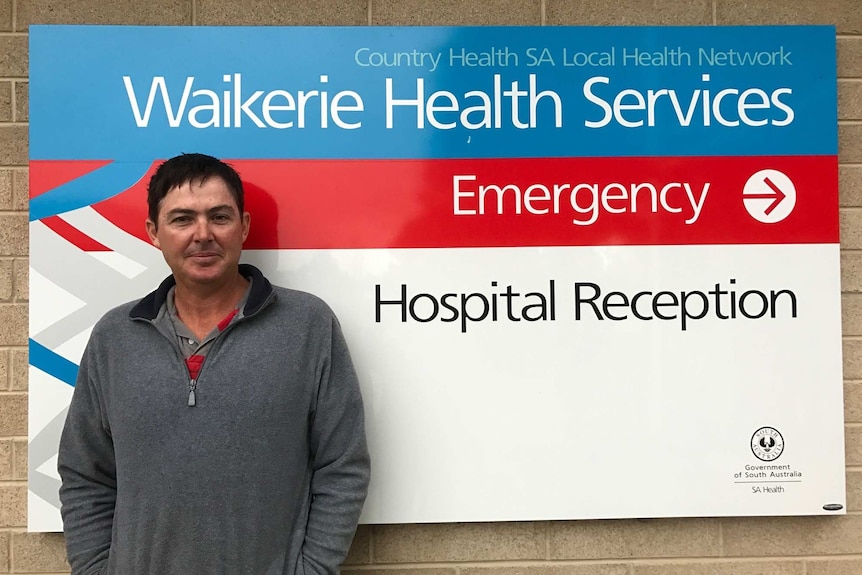 A dark-haired man standing next to a health service sign.