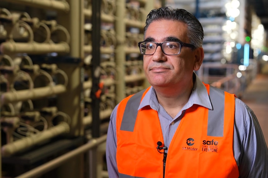 A man with glasses and a high-vis vest stands in an already built desalination plant