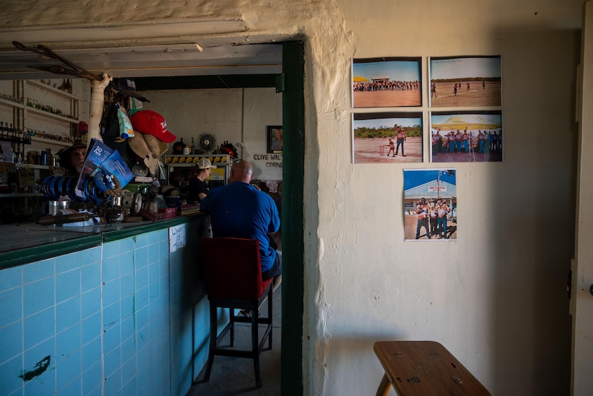 A man sits in an old outback pub, with pictures of times gone by on the wall