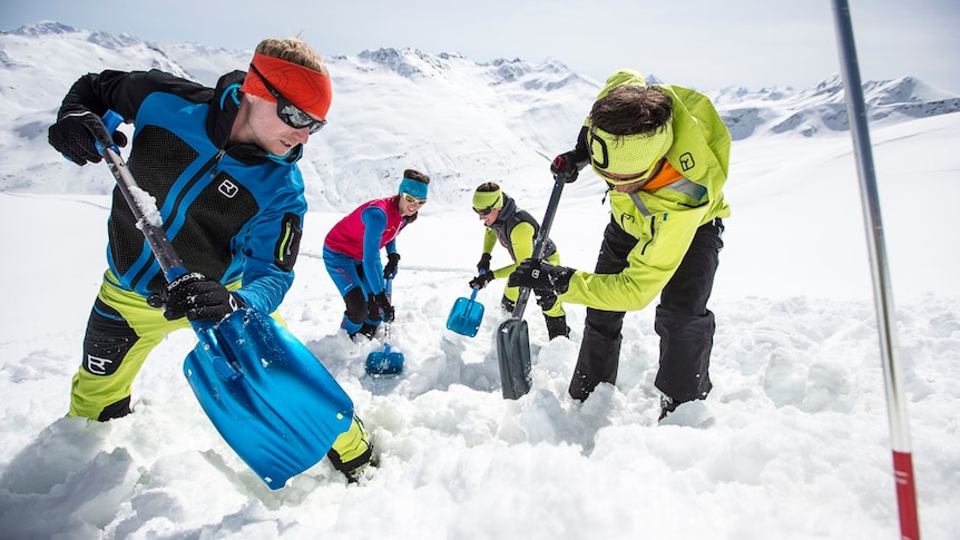 Four mountaineers digging snow with shovels in a snow-covered alpine landscape
