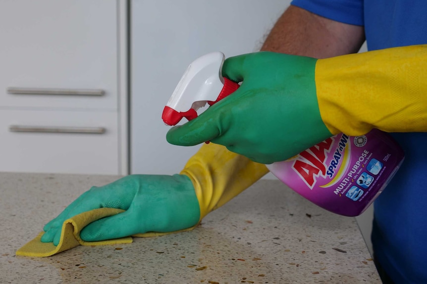 A man wipes a bench top wearing gloves.