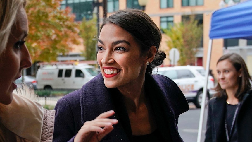 Smiling Alexandria Ocasio-Cortez looks to crowd as she walks