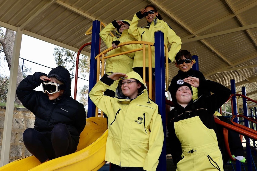 A group of school children in yellow weatherproof clothing on playground equipment.