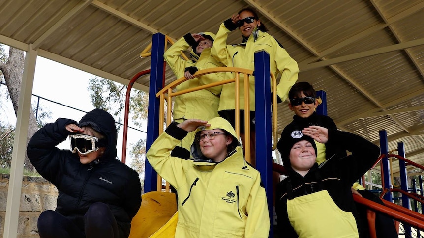 A group of school children in yellow weatherproof clothing on playground equipment.