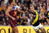 Dustin Martin holds his finger up while running. Lions players around him look disappointed.