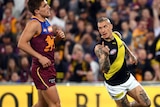 Dustin Martin holds his finger up while running. Lions players around him look disappointed.