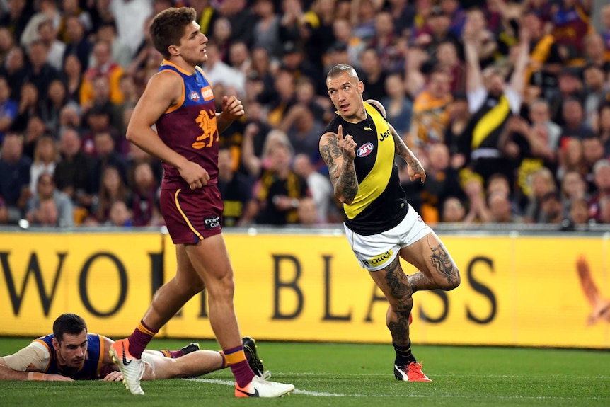 Dustin Martin holds his finger up while running. Lions players around him look disappointed.