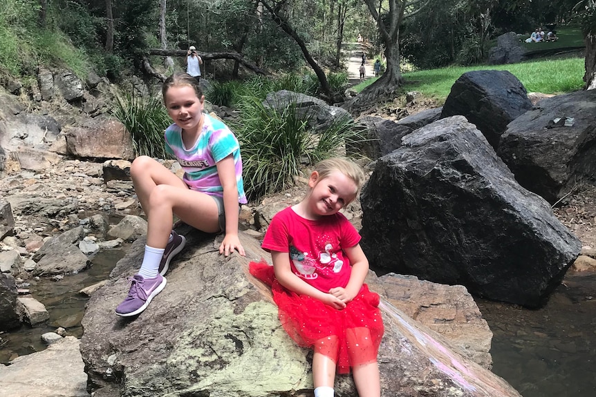 Two young girls sit on rocks near a creek