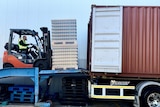 A forklift loads a pallet of goods into a shipping container.