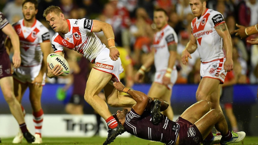 Matthew Dufty attempts to run with the ball, but Apisai Koroisau, lying on his back, has hold of Dufty's shorts.