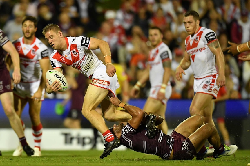 Matthew Dufty attempts to run with the ball, but Apisai Koroisau, lying on his back, has hold of Dufty's shorts.