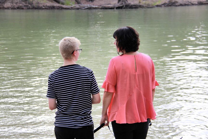 A teenaged boy and his mother look out at a body of water, with their backs to the camera.