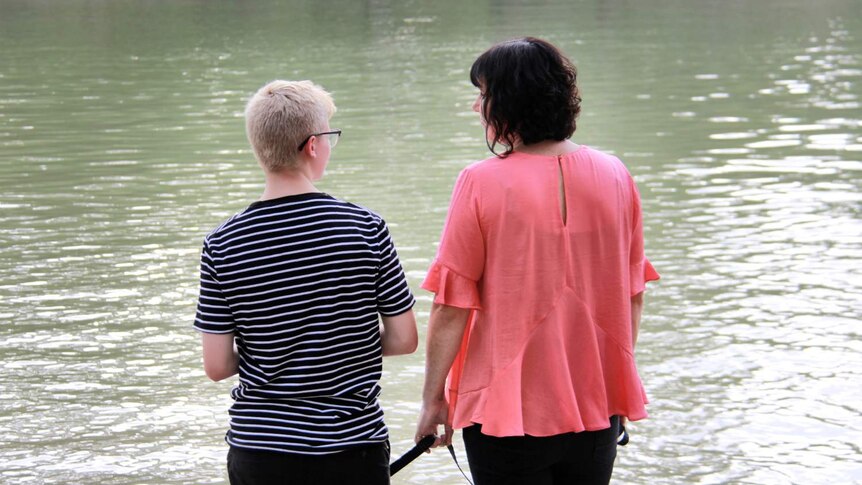 A teenaged boy and his mother look out at a body of water, with their backs to the camera.