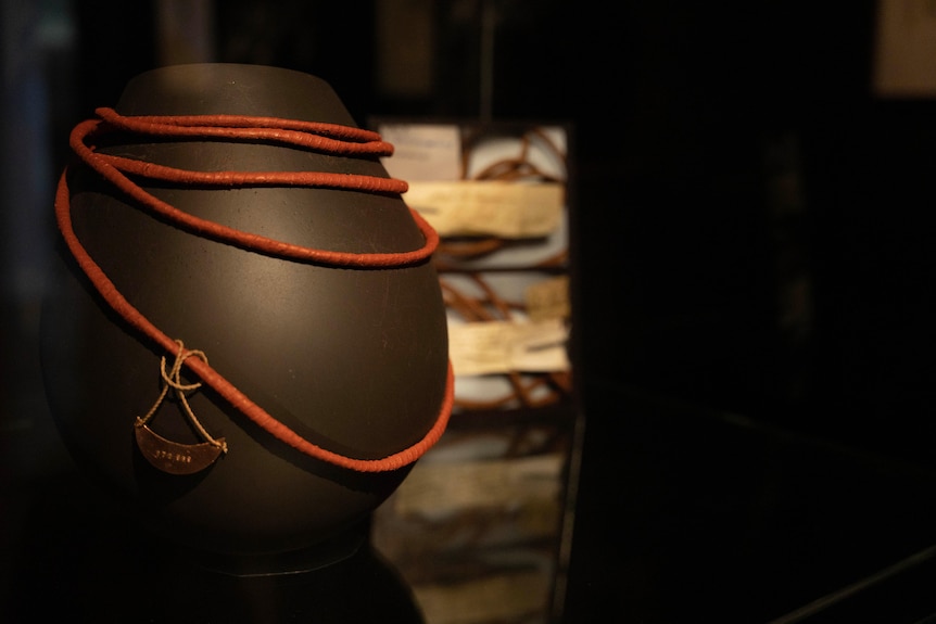 An orange necklace is wrapped around a black vase-shaped object on display.