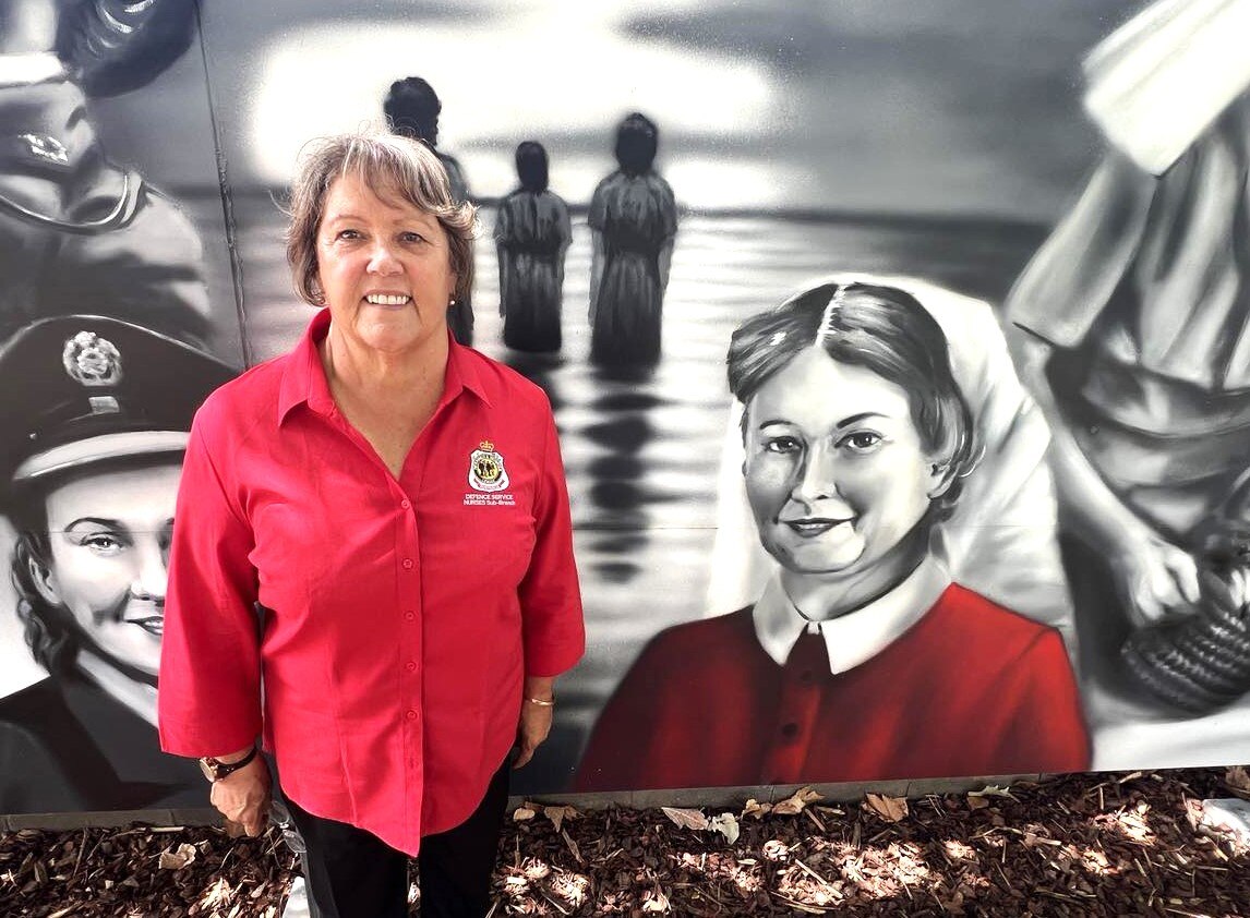 A woman standing next to a painted picture of Sisuter Vivian Bullwinkel 