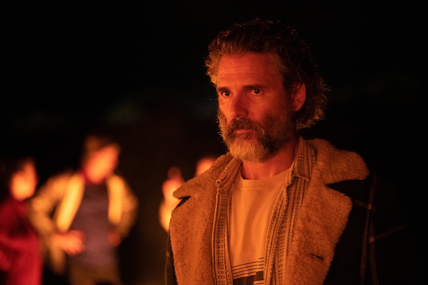 Actor Eric Bana looks off into the distance. He has a beard, medium length hair and is wearing a warm jacket.