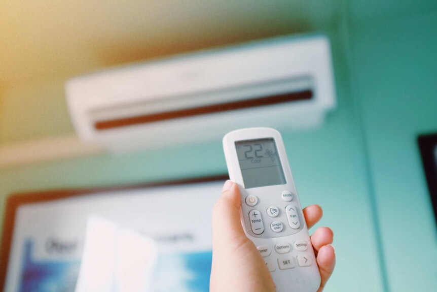 Person pointing remote at reverse cycle air conditioner