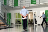 The inside of a prison with a guard standing with his back to camera