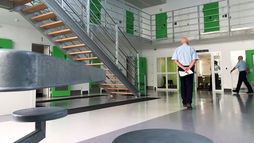 The inside of a prison with a guard standing with his back to camera