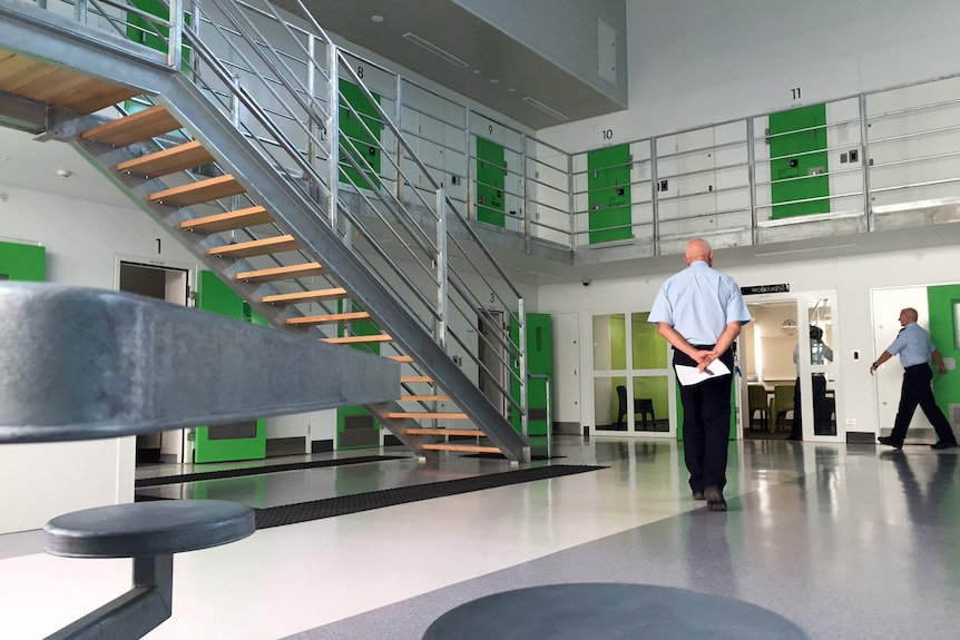 The inside of a prison with a guard standing with his back to camera