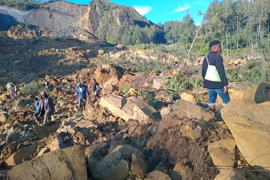 A group of people walk around on some rocks around a mountain.