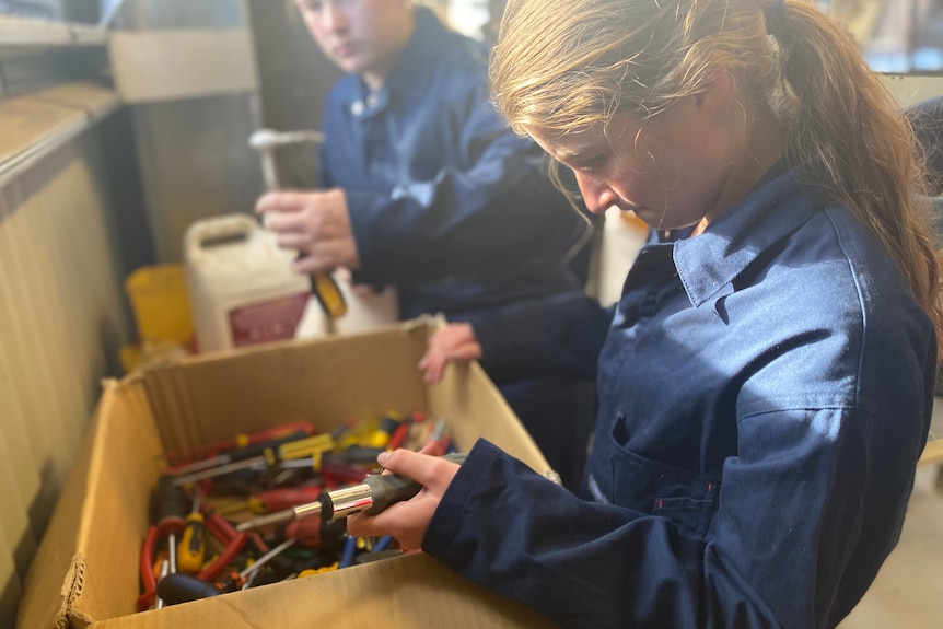 Teenage girl looking for a screw driver in a box which has dozens of them. 