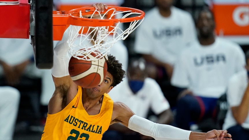 An Australian basketballer hangs on the basket as the ball goes in during a match against the USA. 