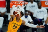 An Australian basketballer hangs on the basket as the ball goes in during a match against the USA. 
