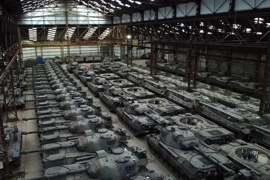 Dozens of German-made Leopard 1 tanks and other armoured vehicles are closely packed together in a large factory. 