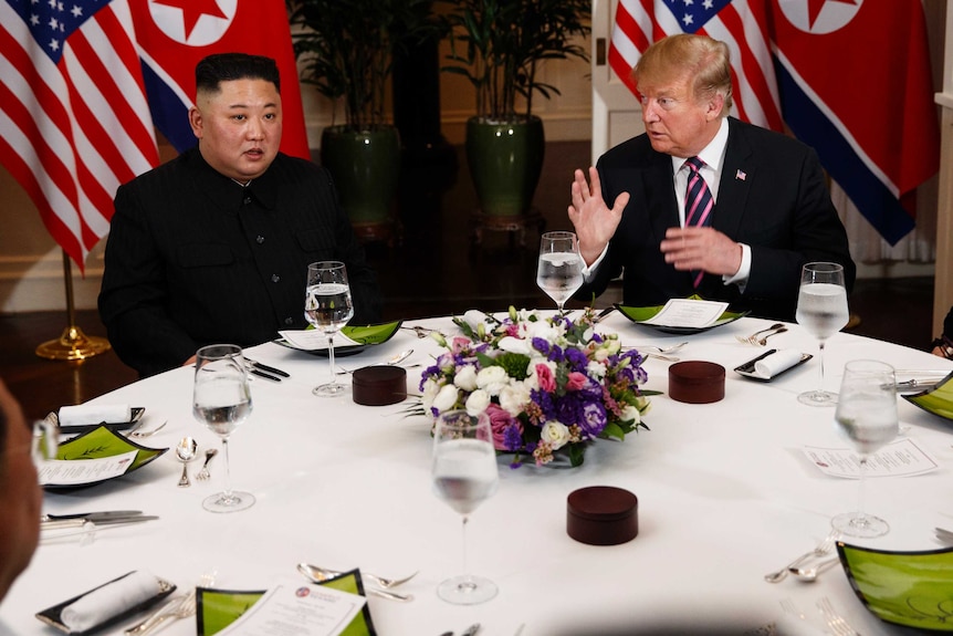 President Donald Trump sits at a table with North Korean leader Kim Jong Un.