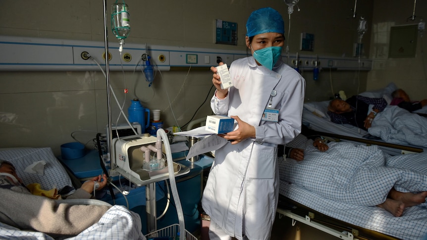 A nurse shows drugs to hospital patients on drips and ventilators.