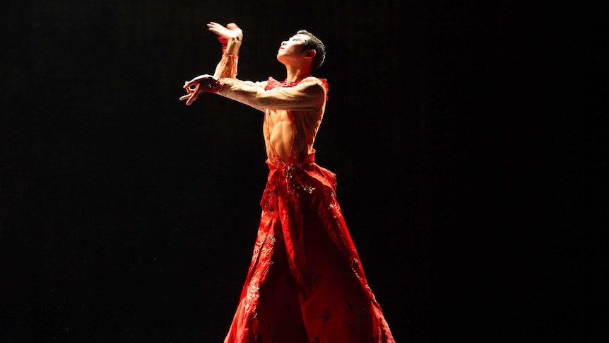 Hu Shenyuan strikes a pose on stage under a spotlight in front of a black backdrop.