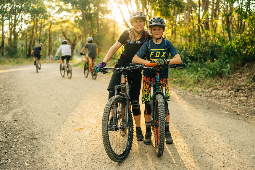 A woman and boy standing on bike with helmets on smiling at camera