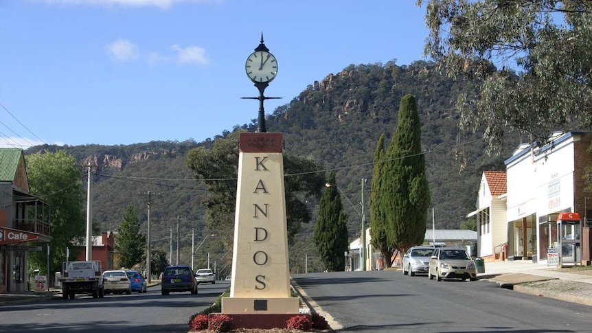 A clock on a pillar with the words Kandos written on it in the middle of the road in a country town