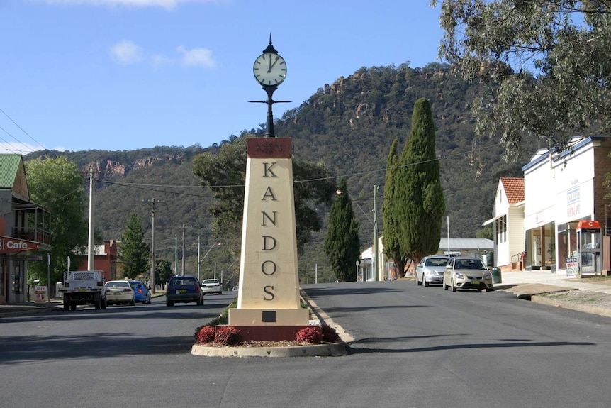 A clock on a pillar with the words Kandos written on it in the middle of the road in a country town