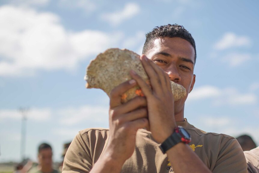 A Royal Tongan Marine blows the conch shell