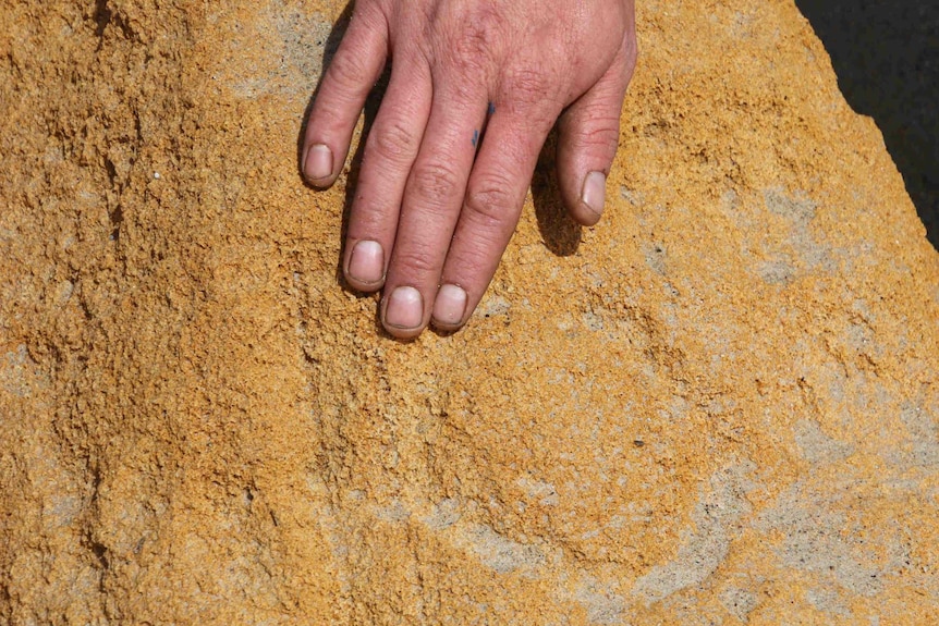 A man's hand touches a rock. Faint circular carvings are visible