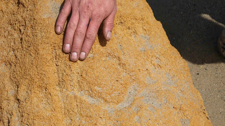 A man's hand touches a rock. Faint circular carvings are visible