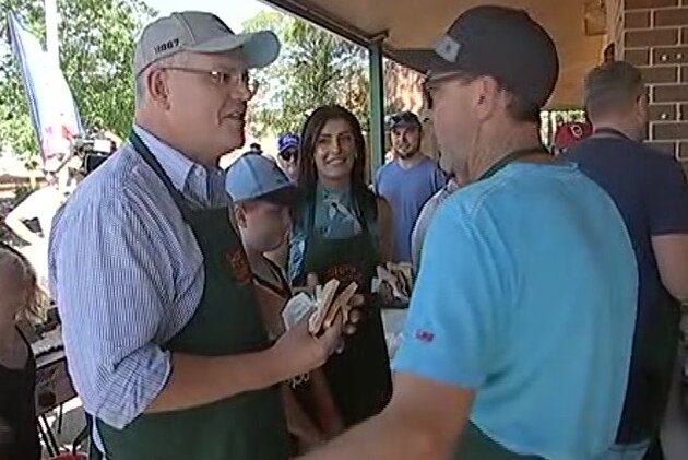 scott morrison holding a sausage sandwich and talking to a man