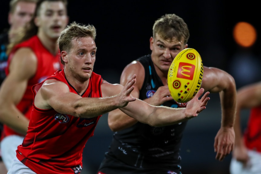 An Essendon AFL player is chased by a Port Adelaide opponent.