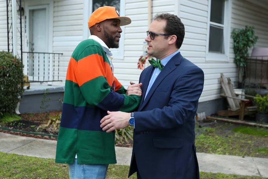 Onrae and Mark embrace while shaking hands on the front lawn of a suburban home