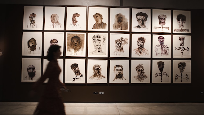 Silhouette of a woman walks in front of artworks by Sidney Nolan. Gloomy.