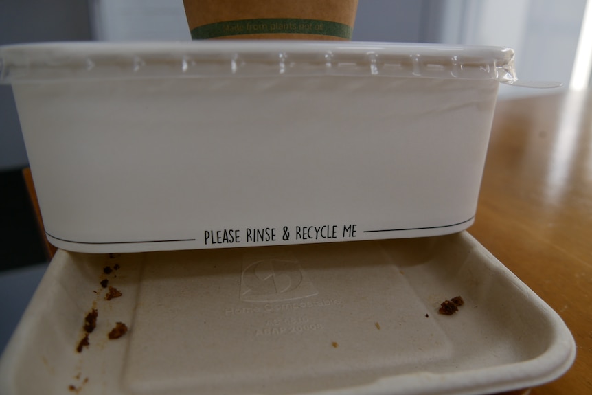 a white cardboard container sitting on top a paper tray with food scraps which says please rinse and recycle me 