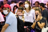 A queue of passengers stand around wearing face masks waiting to board a flight at an airport