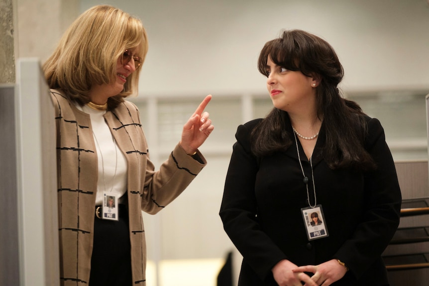 A fair-haired older woman in a plaid jacket wags her finger at a younger, dark-haired woman dressed in black