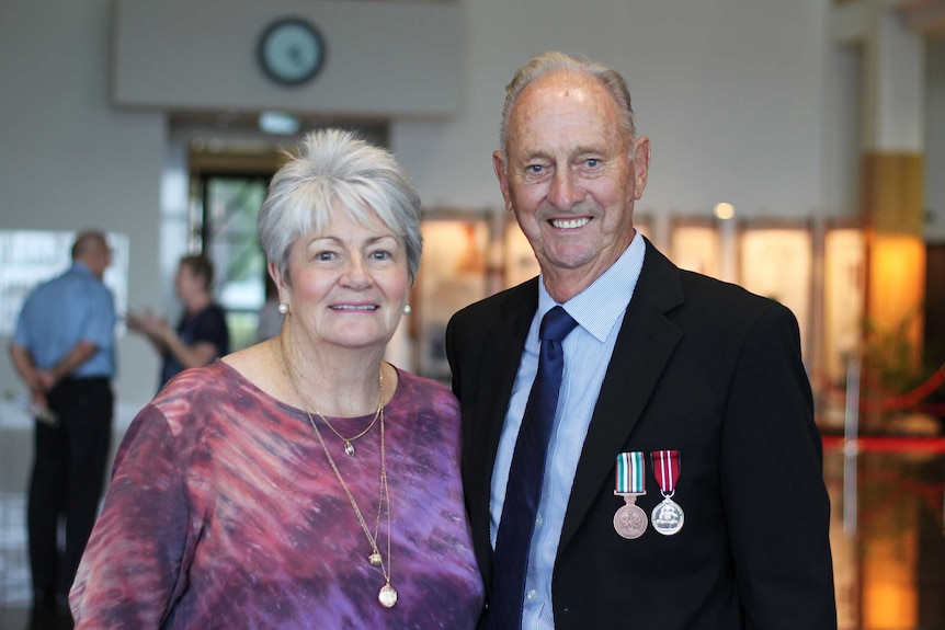 An man decorated in military medals with a  woman at a formal setting.