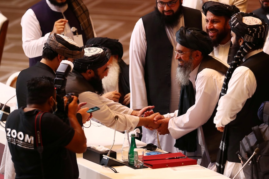 Taliban delegates wearing tradicaitonl clothing and turbans shake hands over a table.